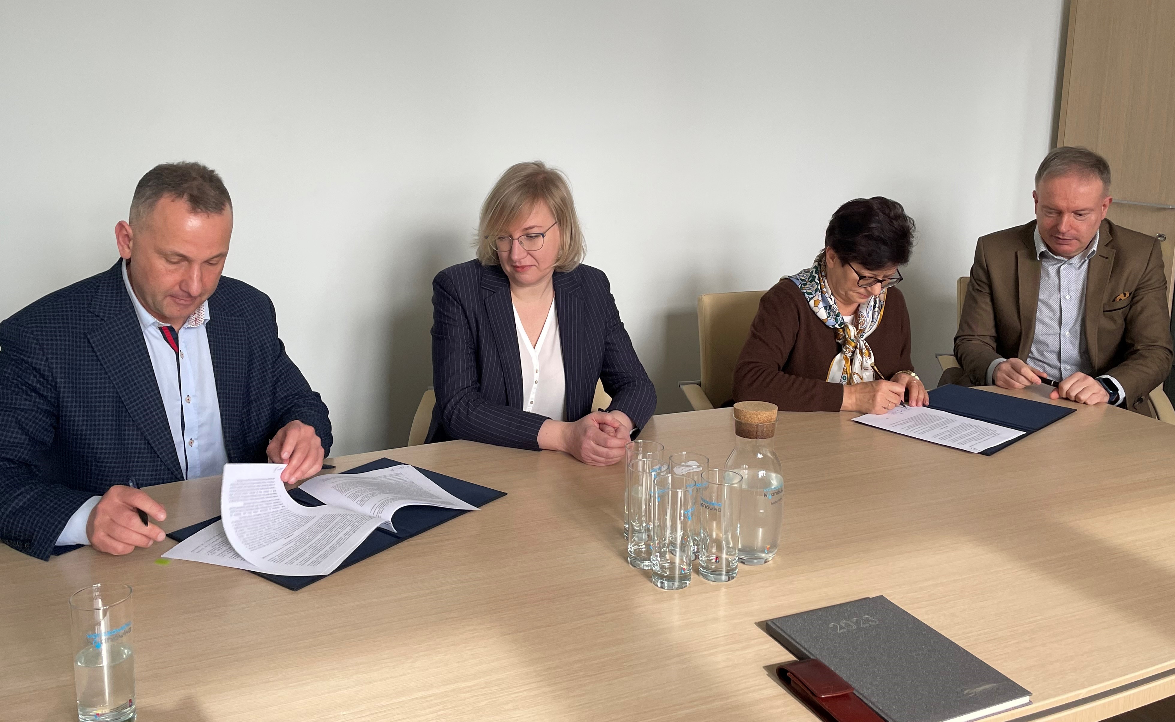 Na zdjęciu przy stole siedza cztery osoby: dwie kobiety i dwóch mężczyzn. Pospisują dokumenty.