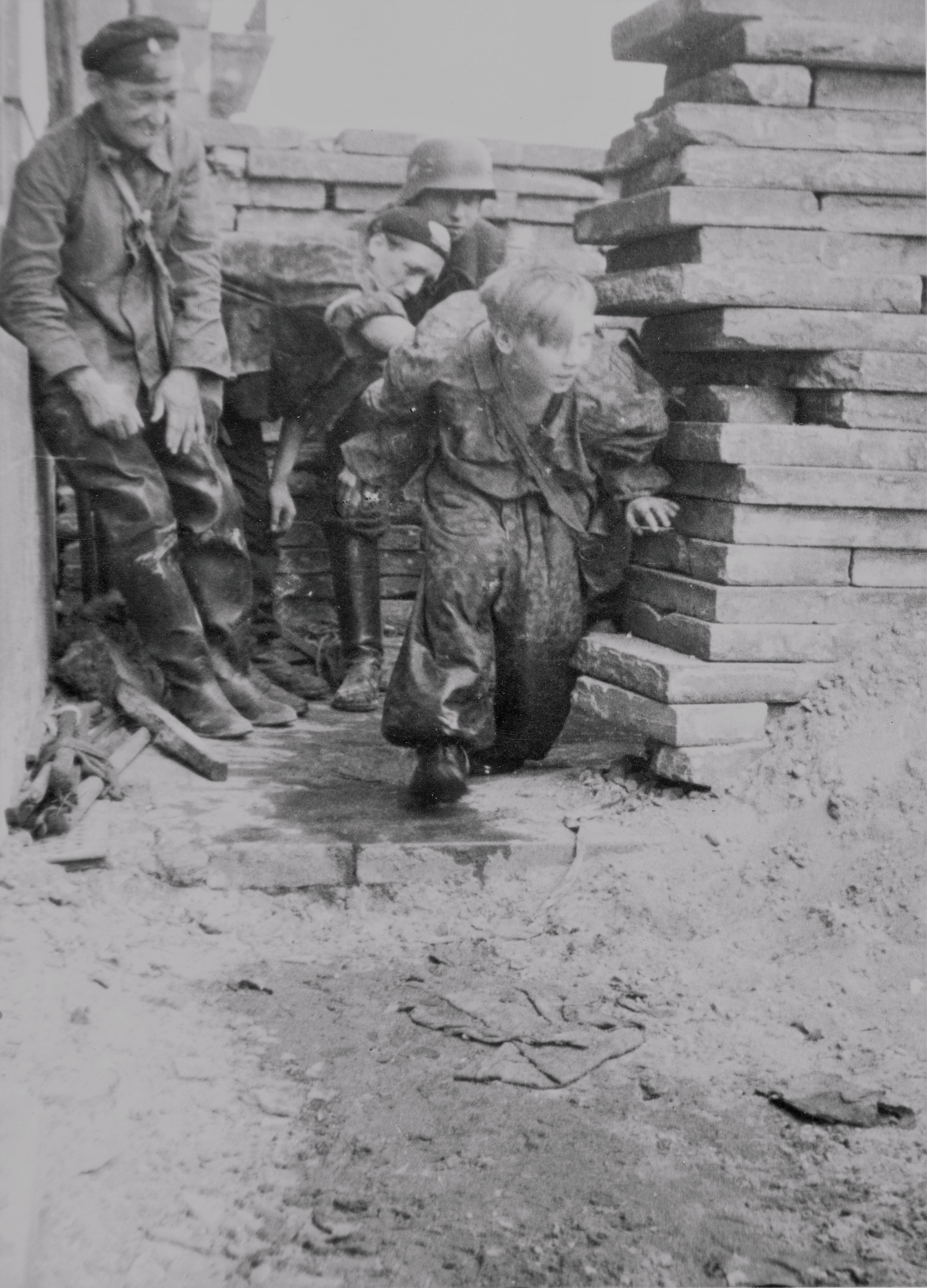 Czarno-biała fotografia archiwalna przedstawiająca powstańców warszawskich, pracownika wodociągów i kanalizacji oraz fragment murów.
