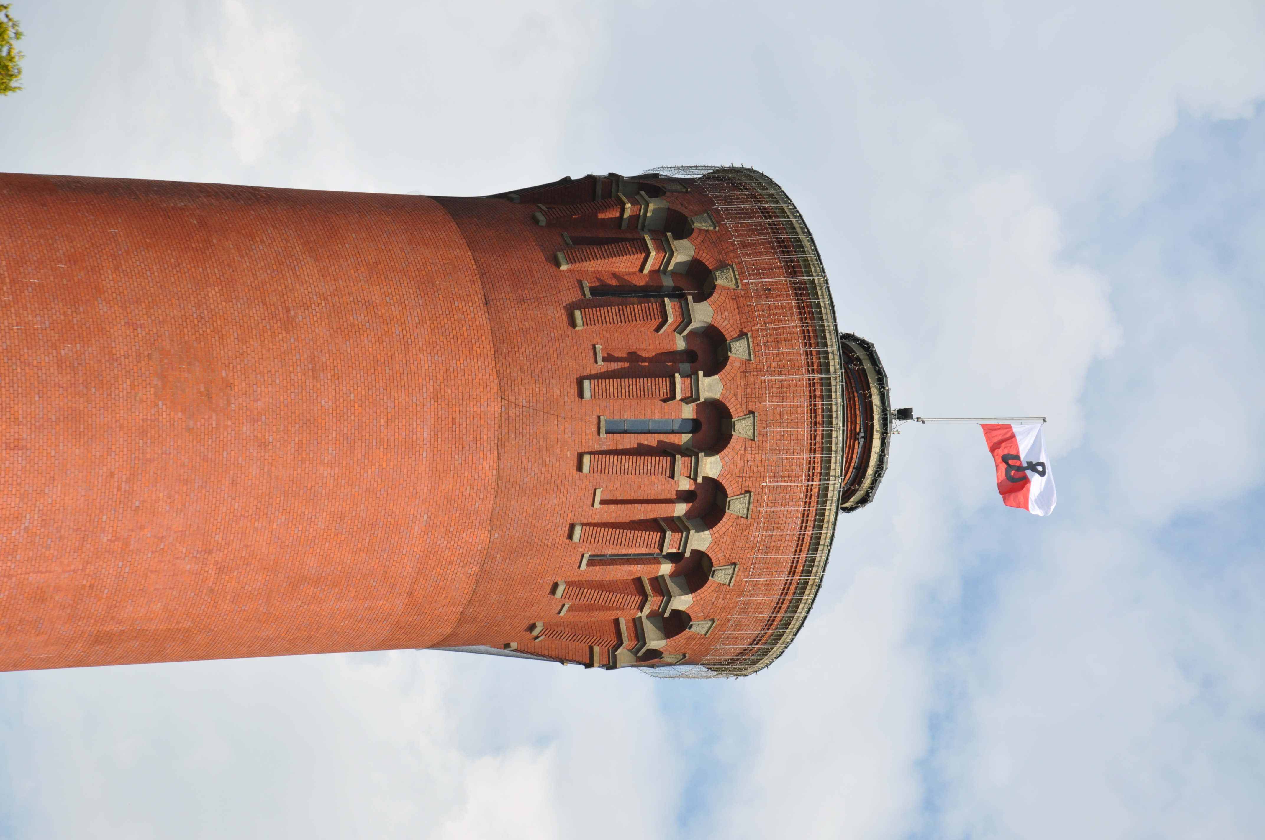 Wierzchołek wieży ciśnień z biało-czerwoną flaga ze znakiem Polski walczącej